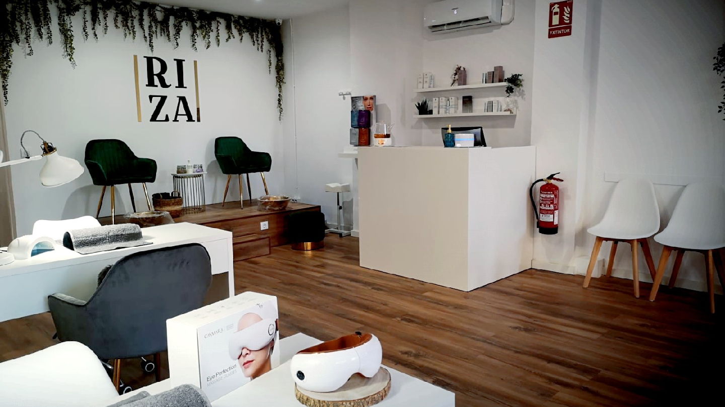 Interior del salón Riza con sillas verdes de terciopelo, mesas de manicura y plantas colgantes