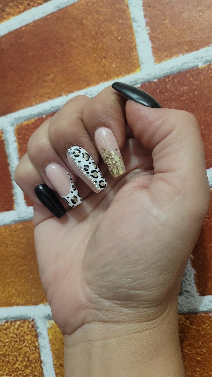 Mano con uñas esculpidas con diseño de leopardo en negro y dorado sobre base nude