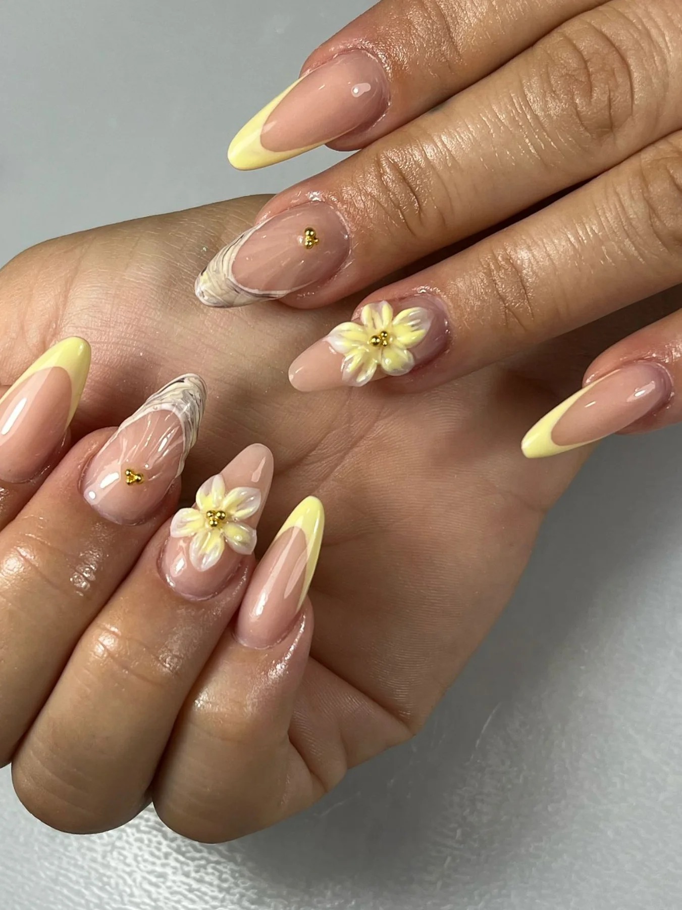 Uñas almendradas con flores amarillas pintadas a mano, French tips amarillos y detalles dorados