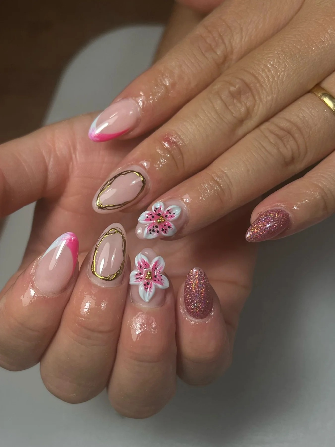 Uñas almendradas con flores blancas y rosas pintadas, contorno dorado y purpurina rosa