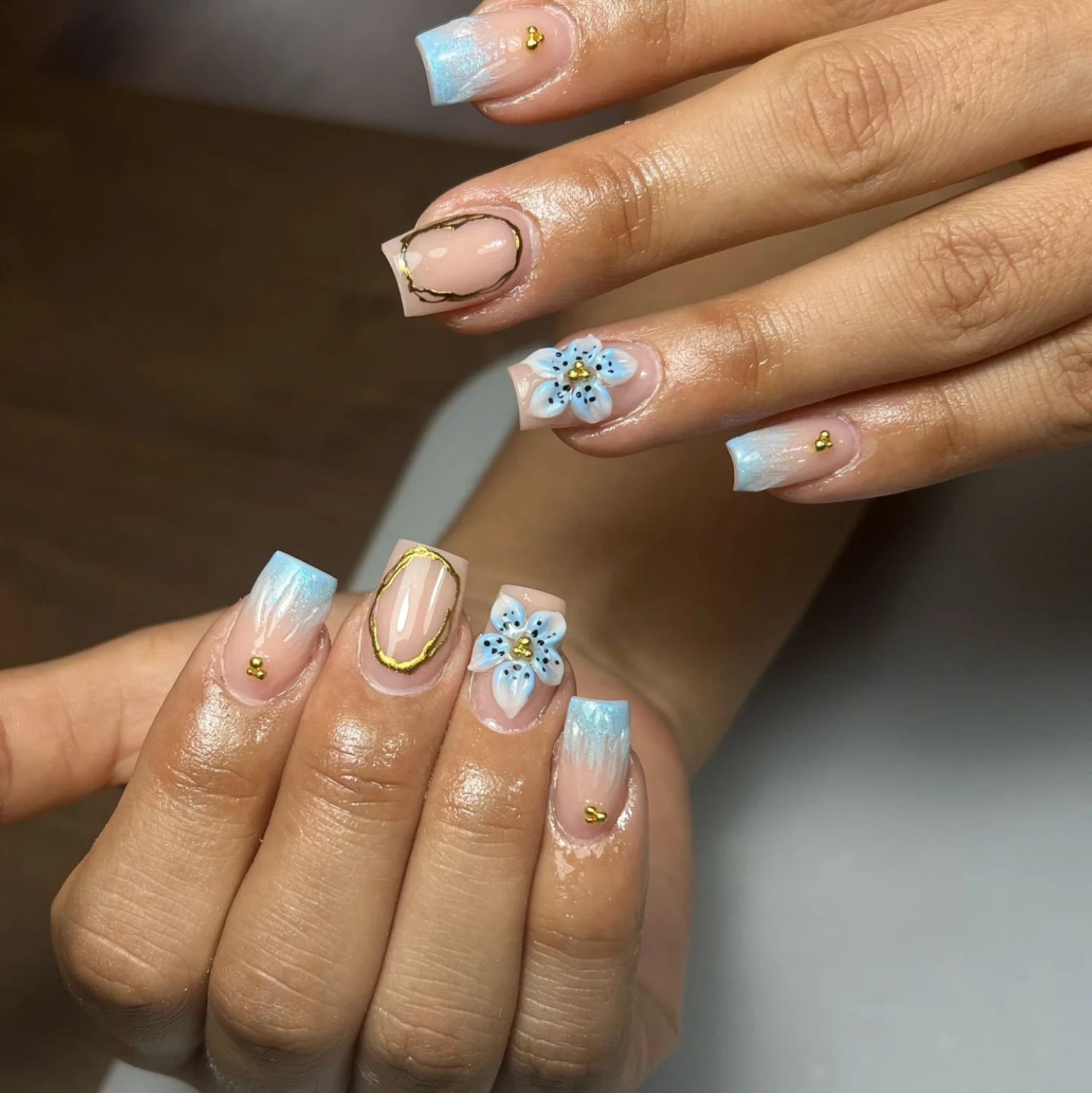 Uñas con flores azul celeste pintadas a mano, French tips azules y detalles dorados