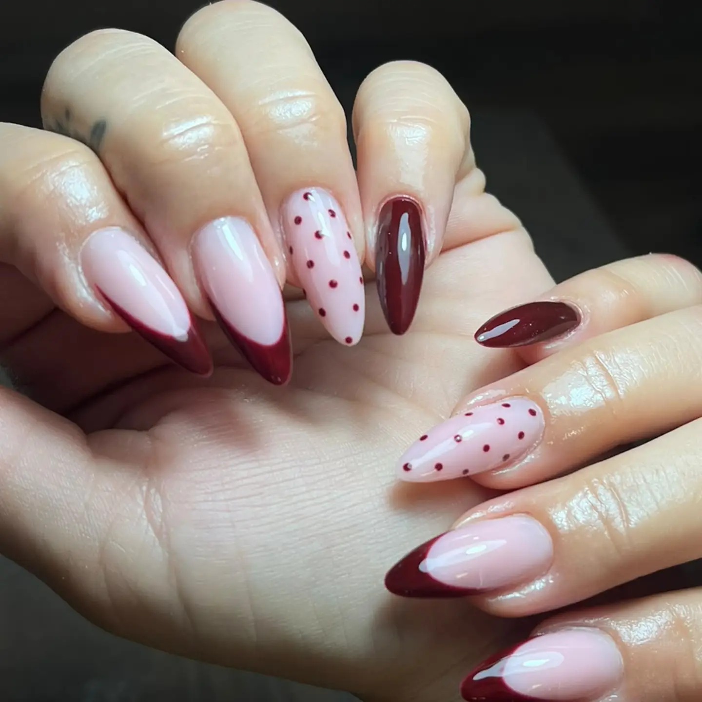 Uñas almendradas con French tips vino tinto y una uña con puntos rojos sobre base nude