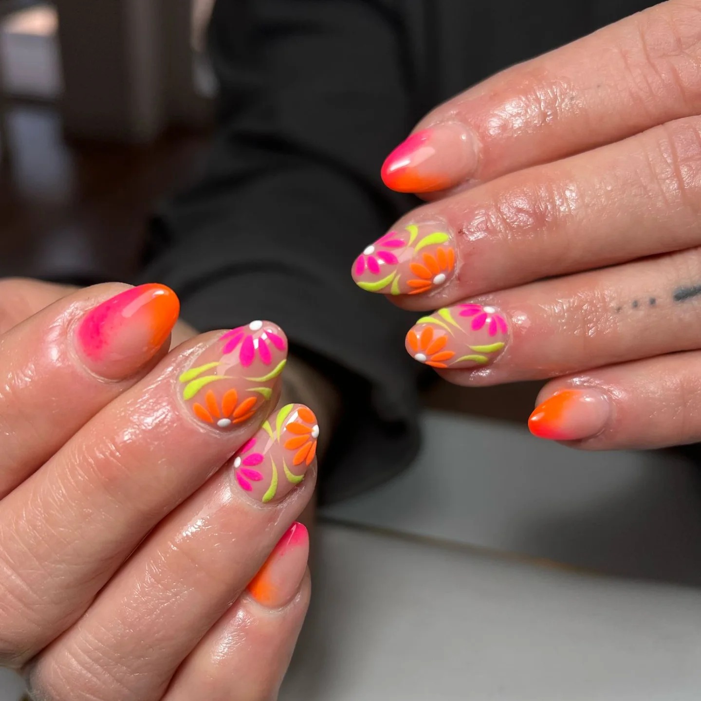 Uñas con degradado de rosa a naranja y flores multicolores en tonos neón