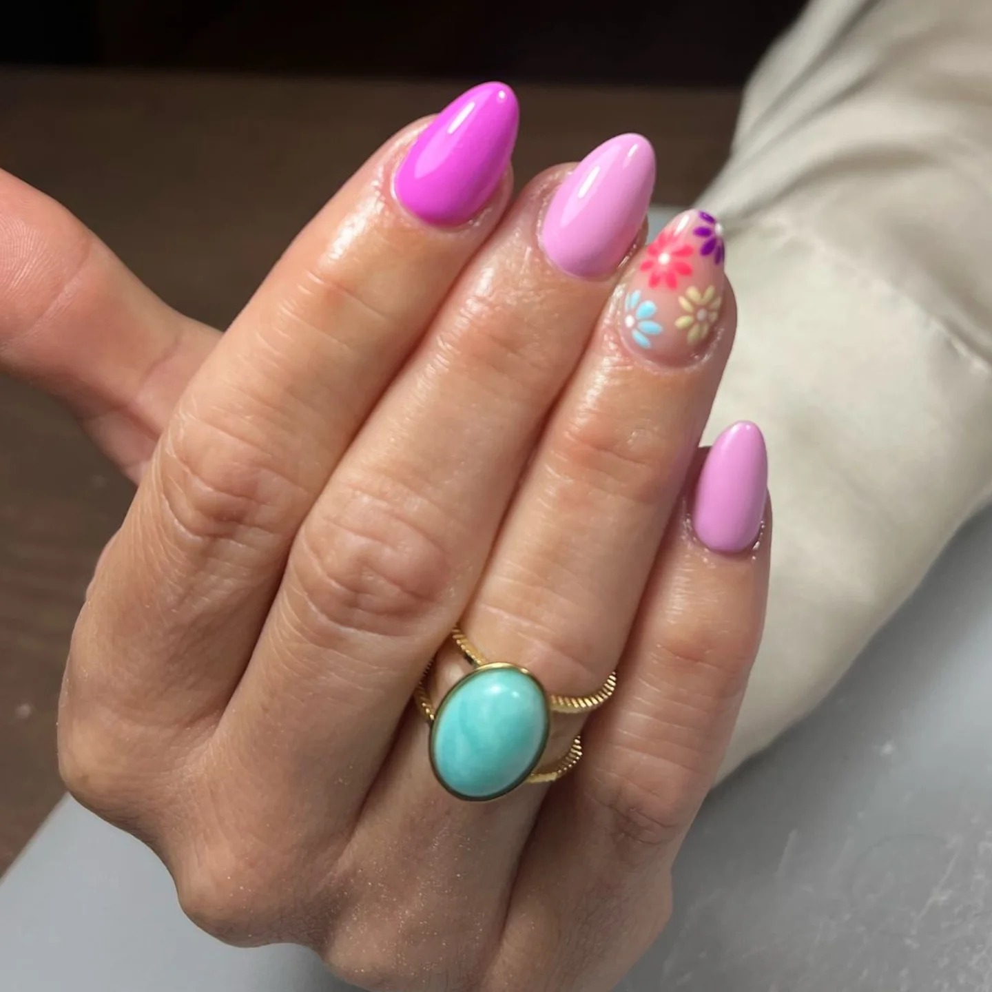 Uñas ovaladas con flores multicolores sobre base transparente y uñas rosas y moradas lisas