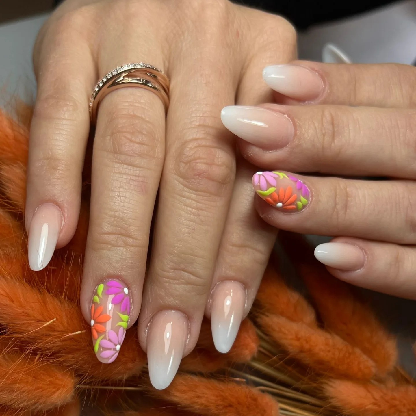 Uñas almendradas beige nude con flores multicolores pintadas en un dedo